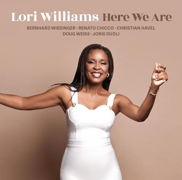 Lori Williams in weißem Kleid, lächelnd, Arme offen. Text: 'Here We Are' und Namen von Personen.