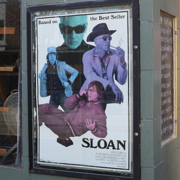 Filmplakat für 'Sloan' mit mehreren Figuren in Blau-, Lila- und Rosatönen. Der Text lautet: 'Basierend auf dem Bestseller'.