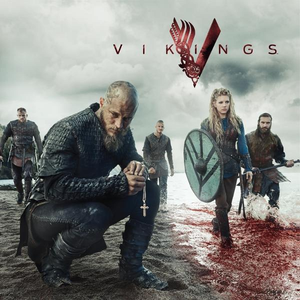 Wikinger-Gruppe am Strand. Einer kniet und hält ein Kreuz. Andere tragen Waffen und Schilde. Der Titel 'Vikings' steht oben.