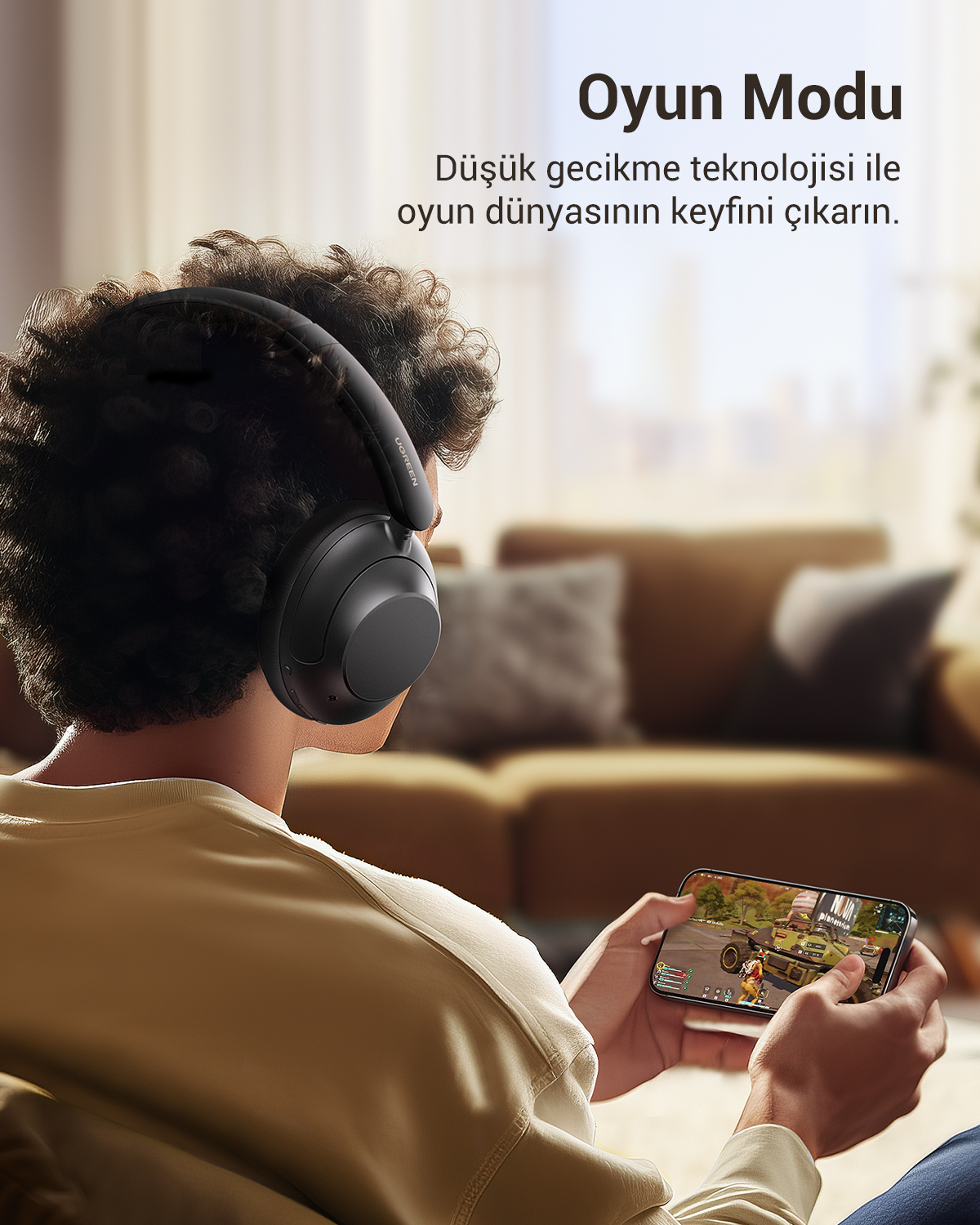 Kulaklık takan bir kişi telefonda oyun oynuyor. Arka planda bir kanepe ve metin katmanı olan bir oturma odası görülüyor.
