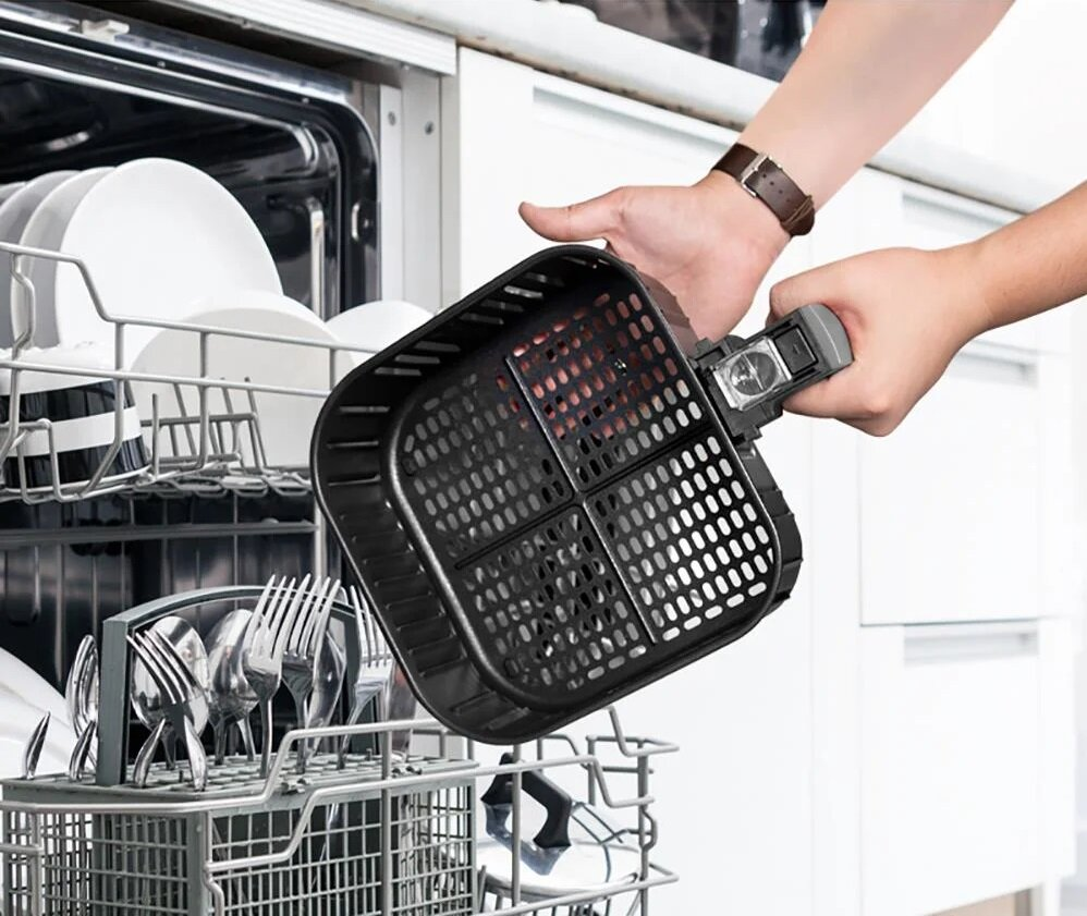 Osoba umieszcza czarny kosz do frytkownicy powietrznej w zmywarce. Naczynia i sztućce są widoczne w zmywarce.