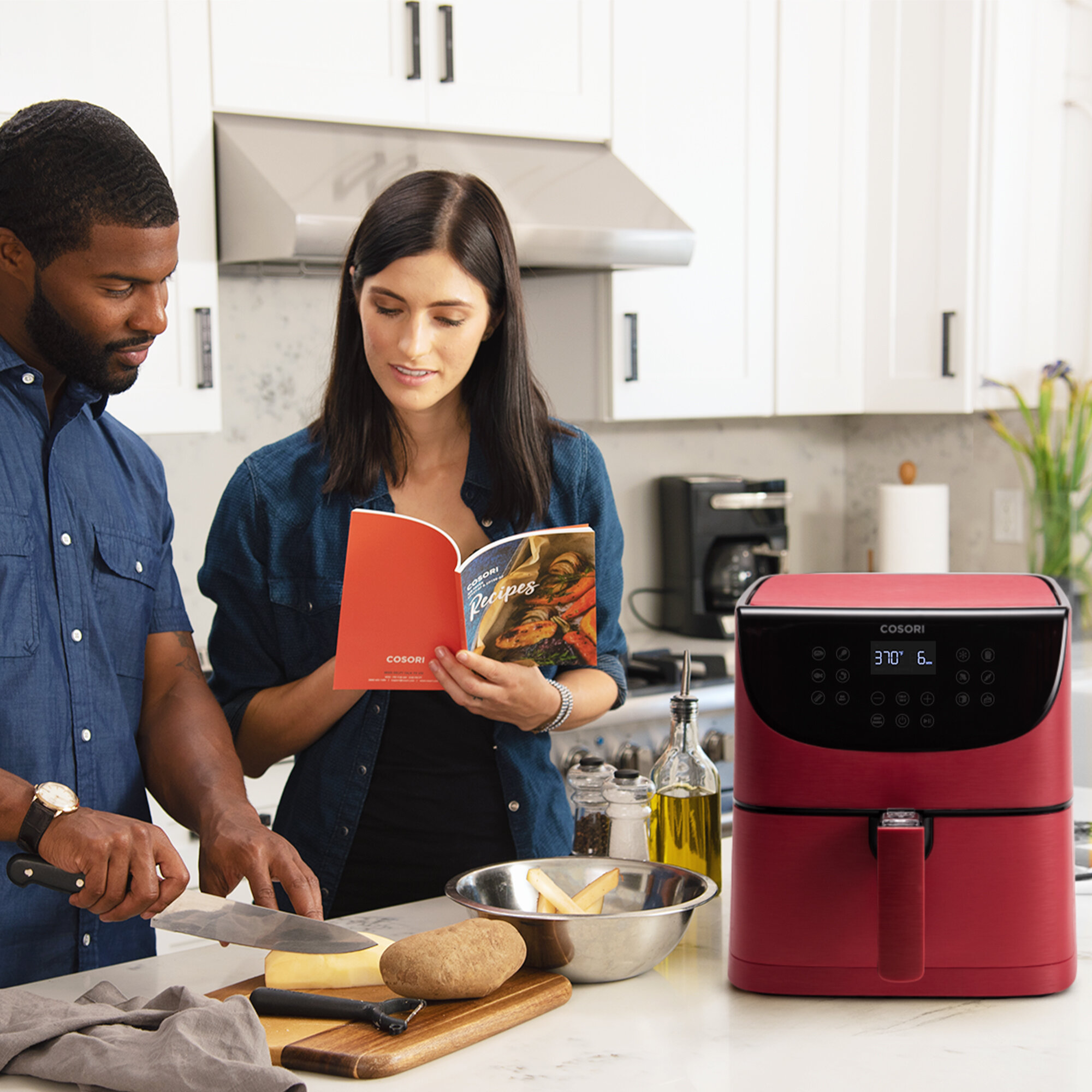 Mężczyzna kroi ser, a kobieta czyta książkę kucharską. Na blacie stoi czerwona frytkownica. Otoczenie kuchni.