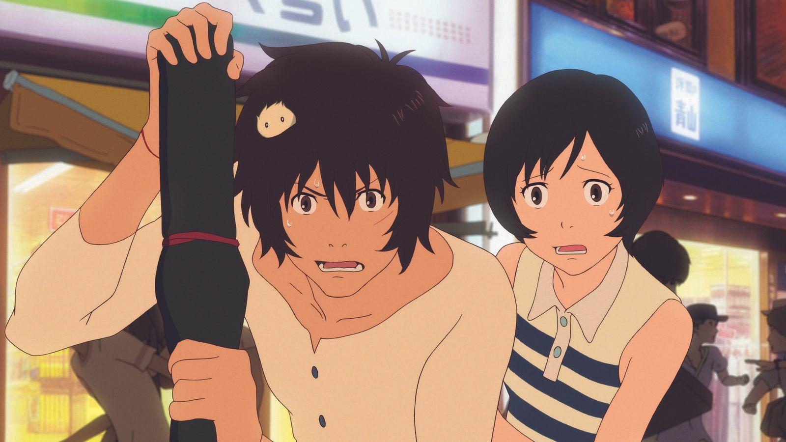 Zwei Anime-Charaktere sehen geschockt aus, einer hält ein schwarzes Objekt. Der Hintergrund zeigt eine Straße mit Geschäften.