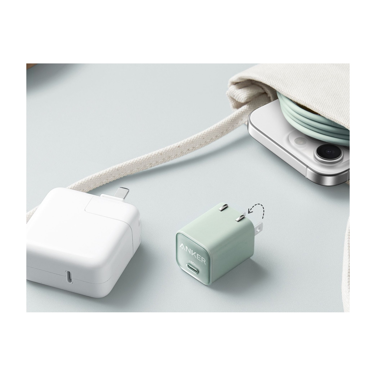 Caricabatterie Anker, caricabatterie bianco e telefono con cavo su una superficie blu. Sono presenti anche un cinturino e un tessuto bianchi.