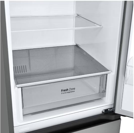 Wnętrze otwartej lodówki. Widoczne półki, półka z siatki i przezroczysta szuflada z napisem 'Fresh Zone Fruit & Vegetables'.