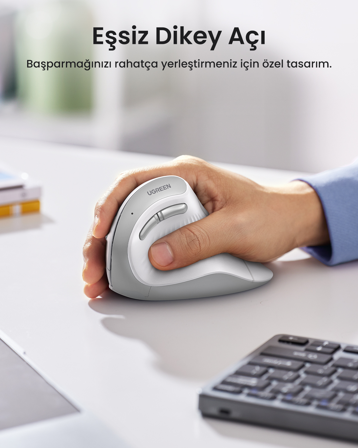 Bir kişinin eli beyaz ve gri ergonomik bir fare tutuyor. Arka planda Türkçe metin ve bir klavye var.