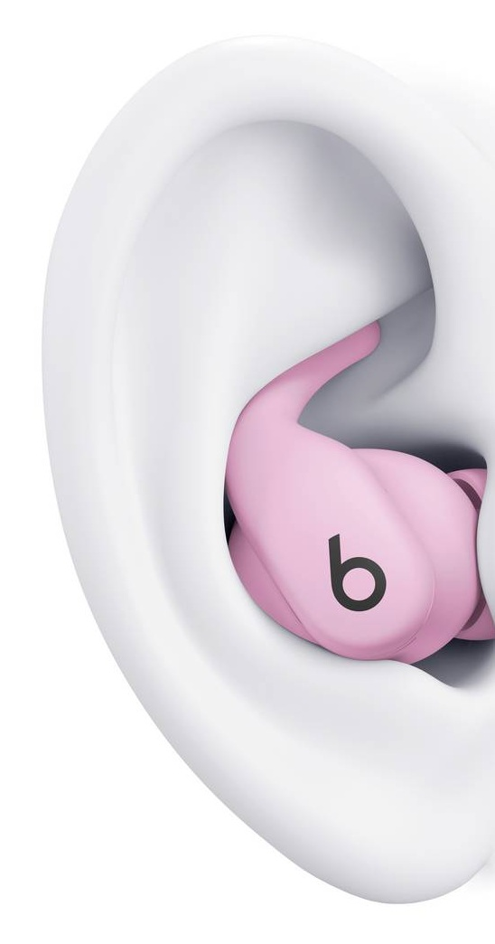 Zbliżenie na jasnoróżową słuchawkę douszną wewnątrz białego ucha. Słuchawka ma czarne logo 'b'. Ucho jest częściowo widoczne.