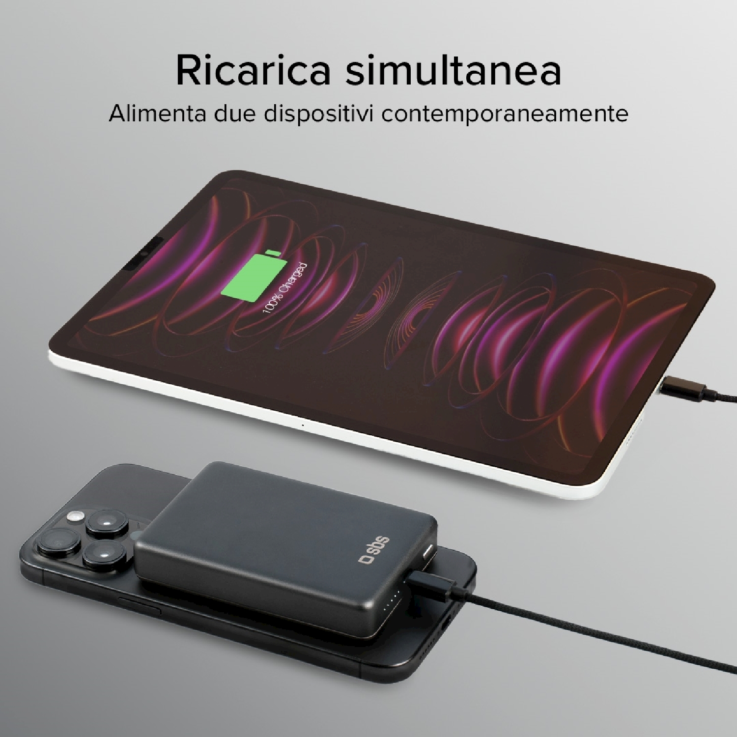 Un tablet e uno smartphone si stanno caricando contemporaneamente. Un power bank è sul telefono. Il tablet mostra 100% caricato.