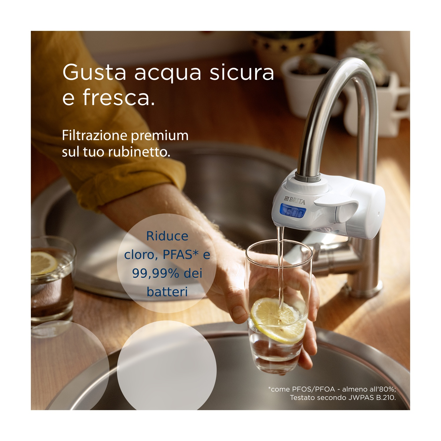 Una mano versa l'acqua da un filtro del rubinetto in un bicchiere con limone. Il testo dice: Goditi acqua sicura e fresca e riduce il cloro.