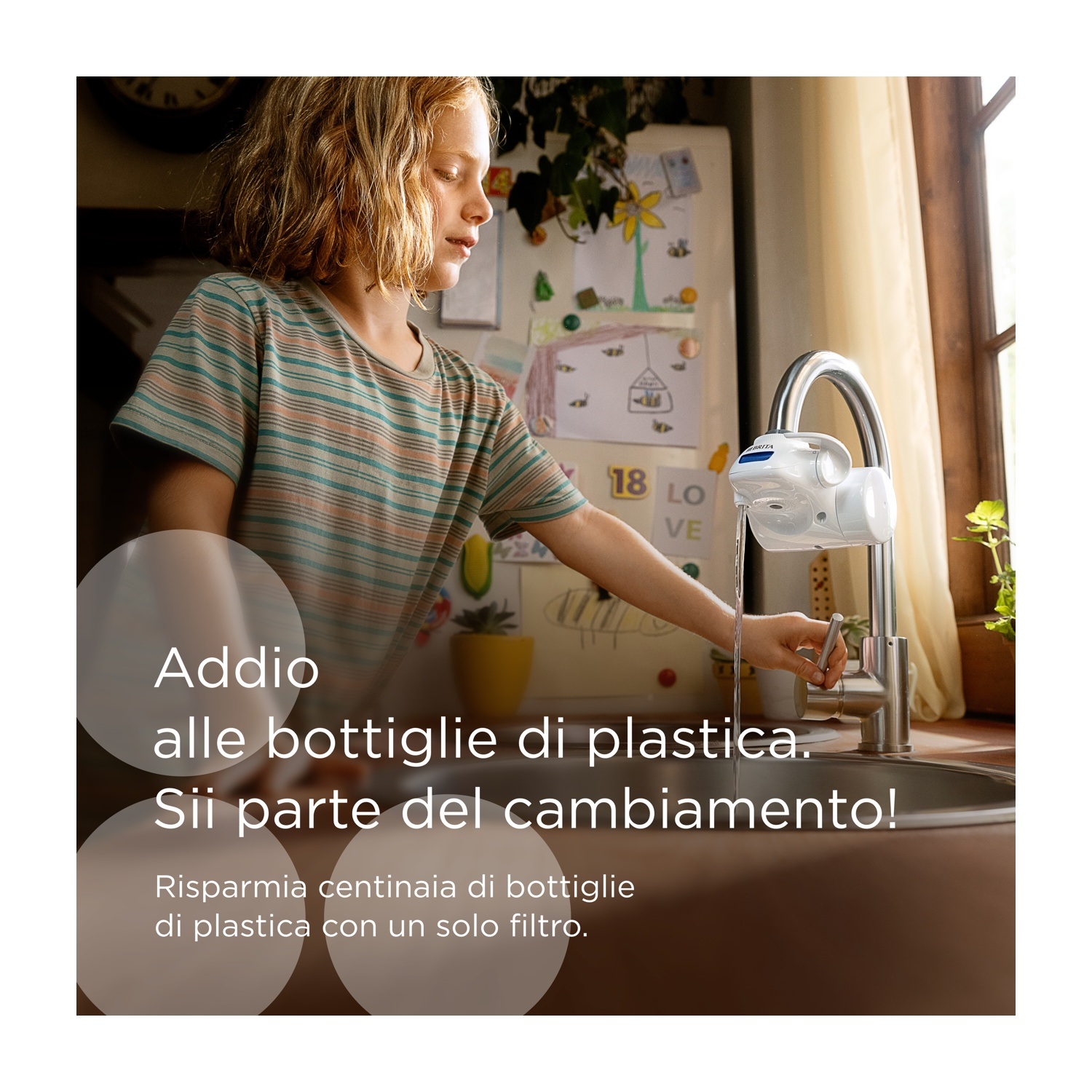 Un bambino riempie un bicchiere d'acqua da un rubinetto con filtro. Lo sfondo mostra una cucina.