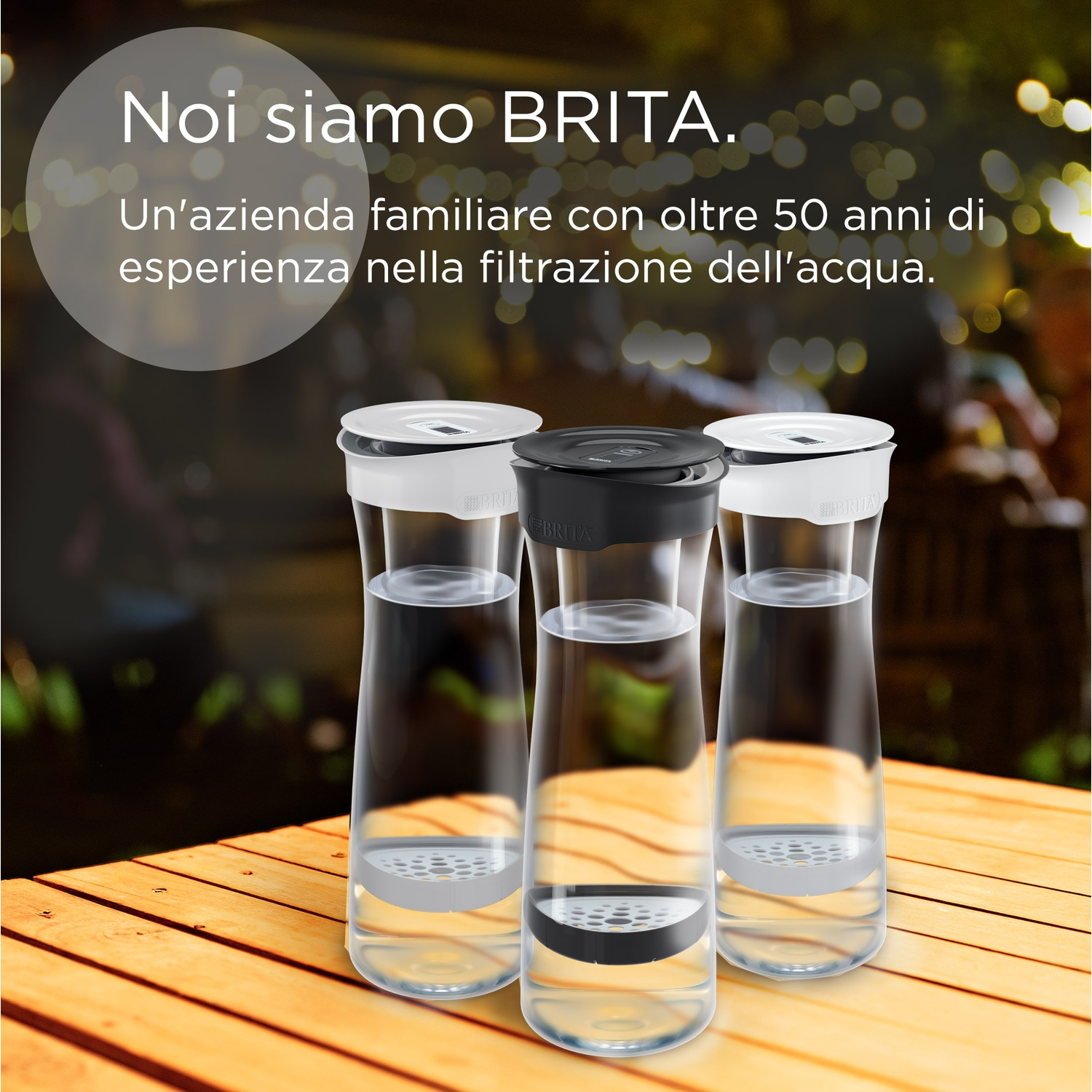 Tre caraffe d'acqua, coperchi bianchi e neri, su un tavolo di legno. Testo: Noi siamo BRITA. Un'azienda familiare con oltre 50 anni di esperienza...