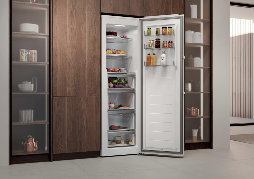 Ein offener Kühlschrank mit Essen im Inneren, in einer Küche aufgestellt. Auf beiden Seiten befinden sich Holzschränke. Gläser und Flaschen sind sichtbar.