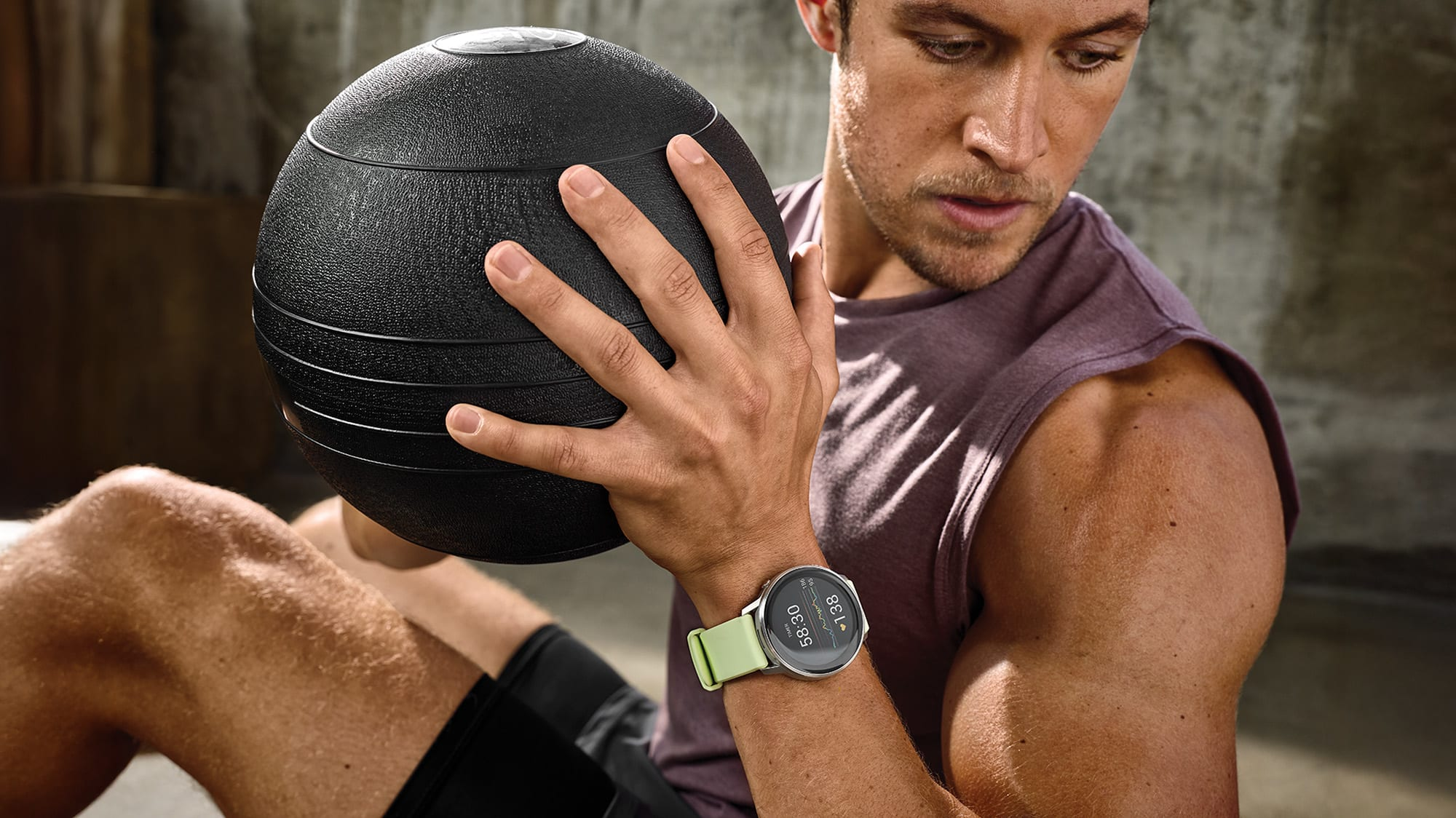 Mężczyzna trzyma czarną piłkę lekarską, nosi smartwatch. Jest na siłowni. Skupienie na ramieniu, piłce i zegarku.