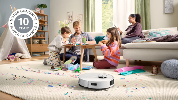Bir aile yerde el işi yapıyor. Bir robot süpürge, konfetilerle kaplı halıyı temizliyor. Bir kadın kanepede kitap okuyor.