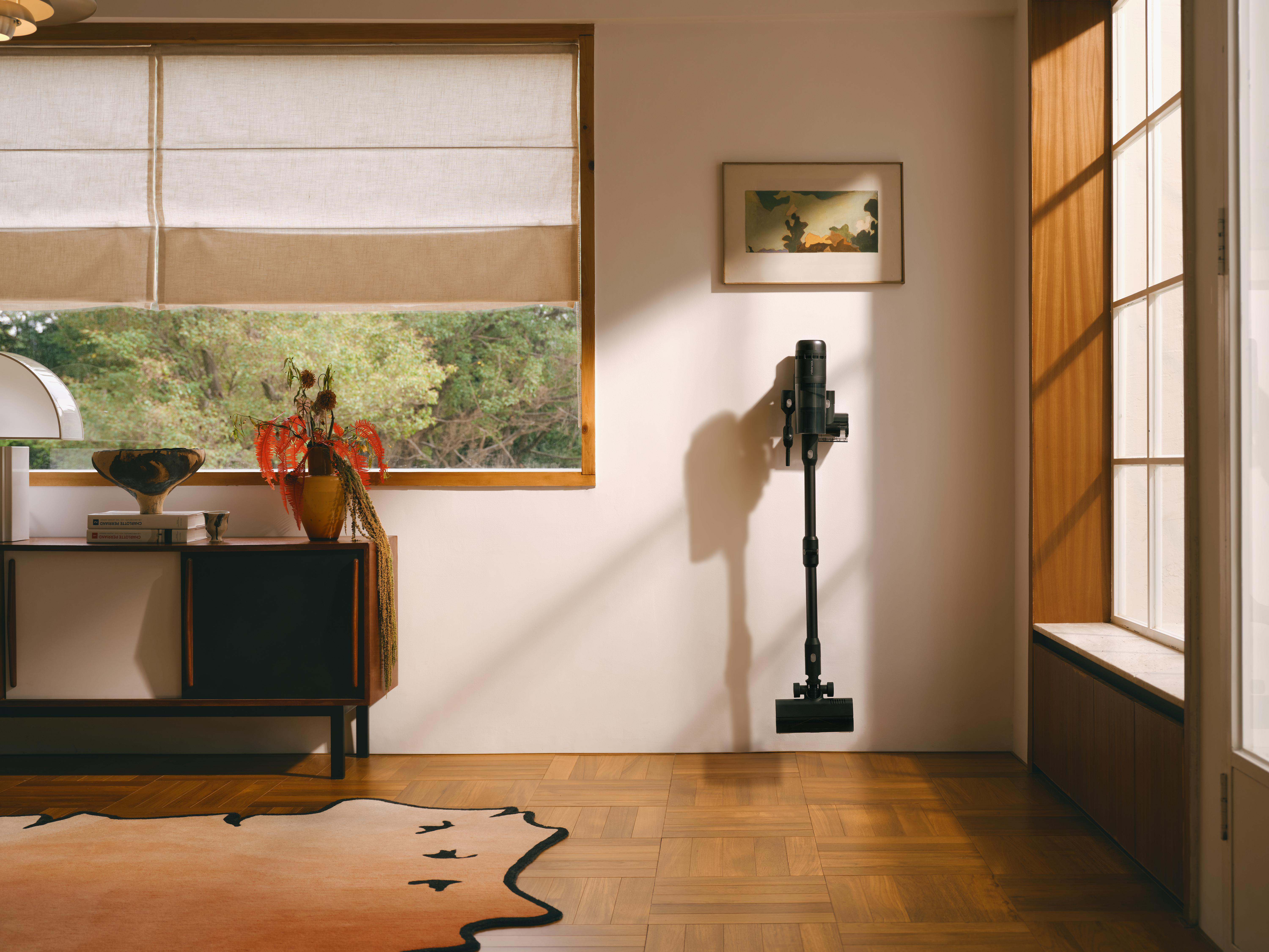 Zimmerinterieur mit einem an der Wand montierten Staubsauger. Ein Teppich, Sideboard und Fenster sind ebenfalls sichtbar.
