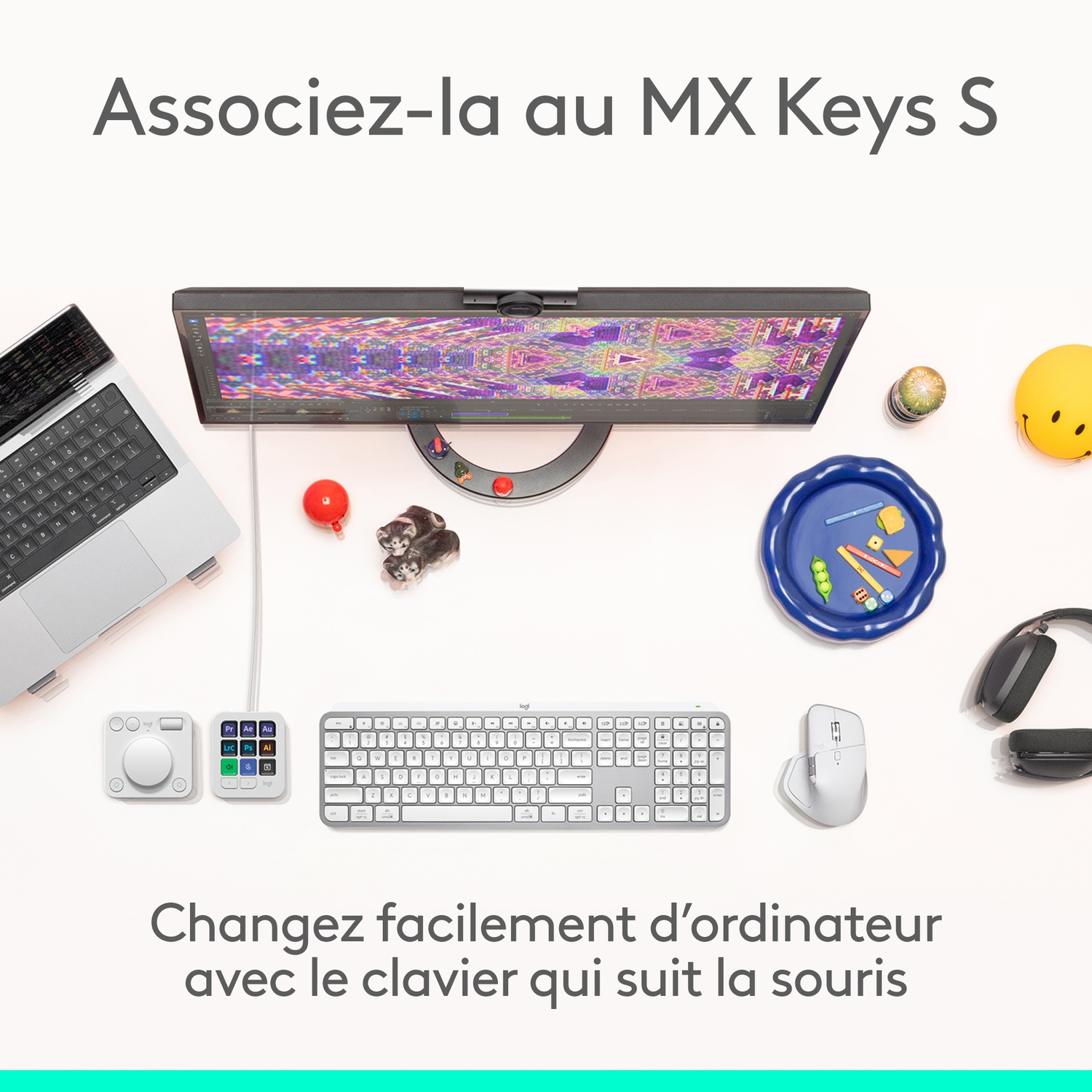 Vue de dessus avec ordinateur portable, moniteur, clavier, souris et accessoires. Un smiley, des chatons jouets et une balle rouge sont également présents.