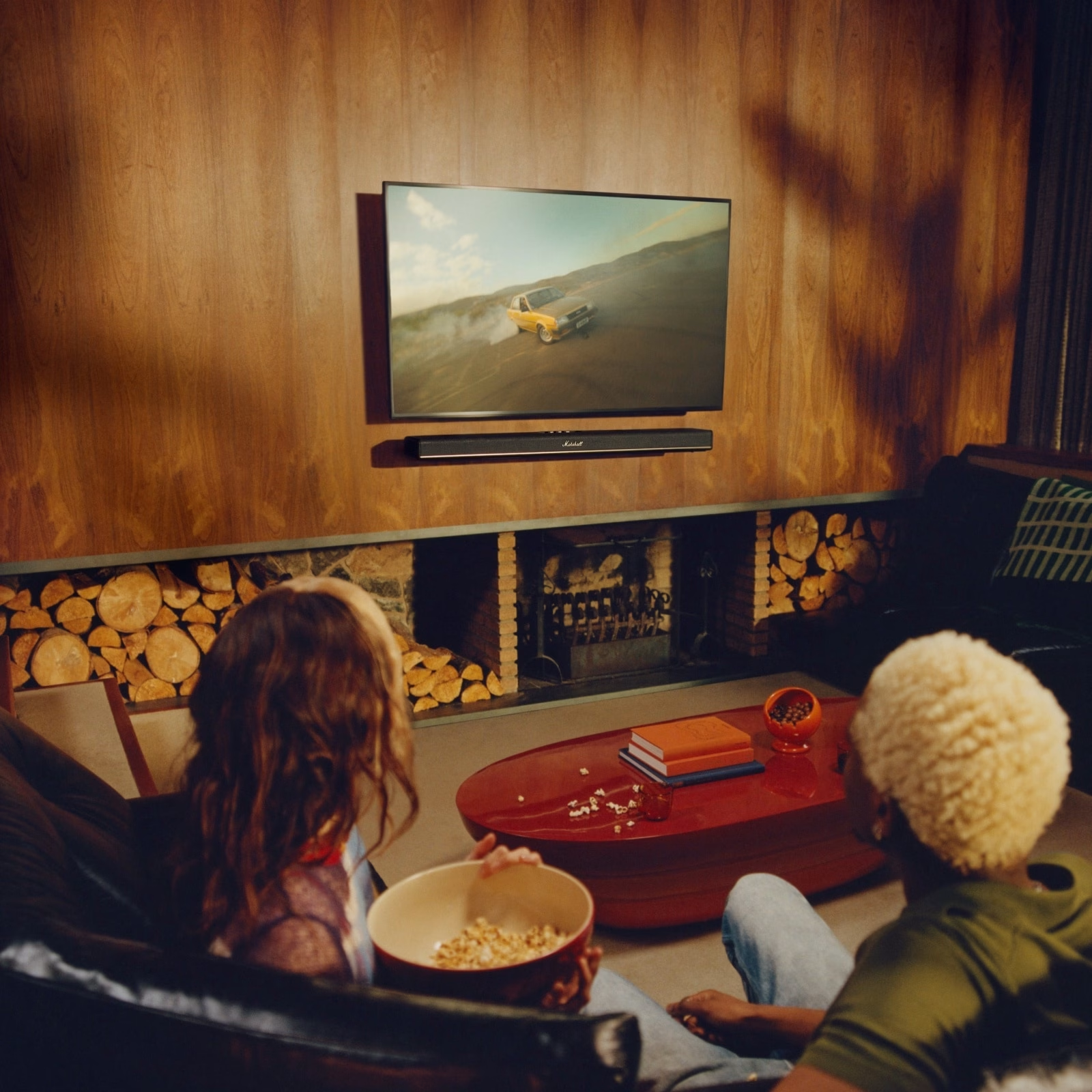 Zwei Personen schauen fern. Das TV zeigt ein driftendes Auto. Eine Schüssel Popcorn im Vordergrund.