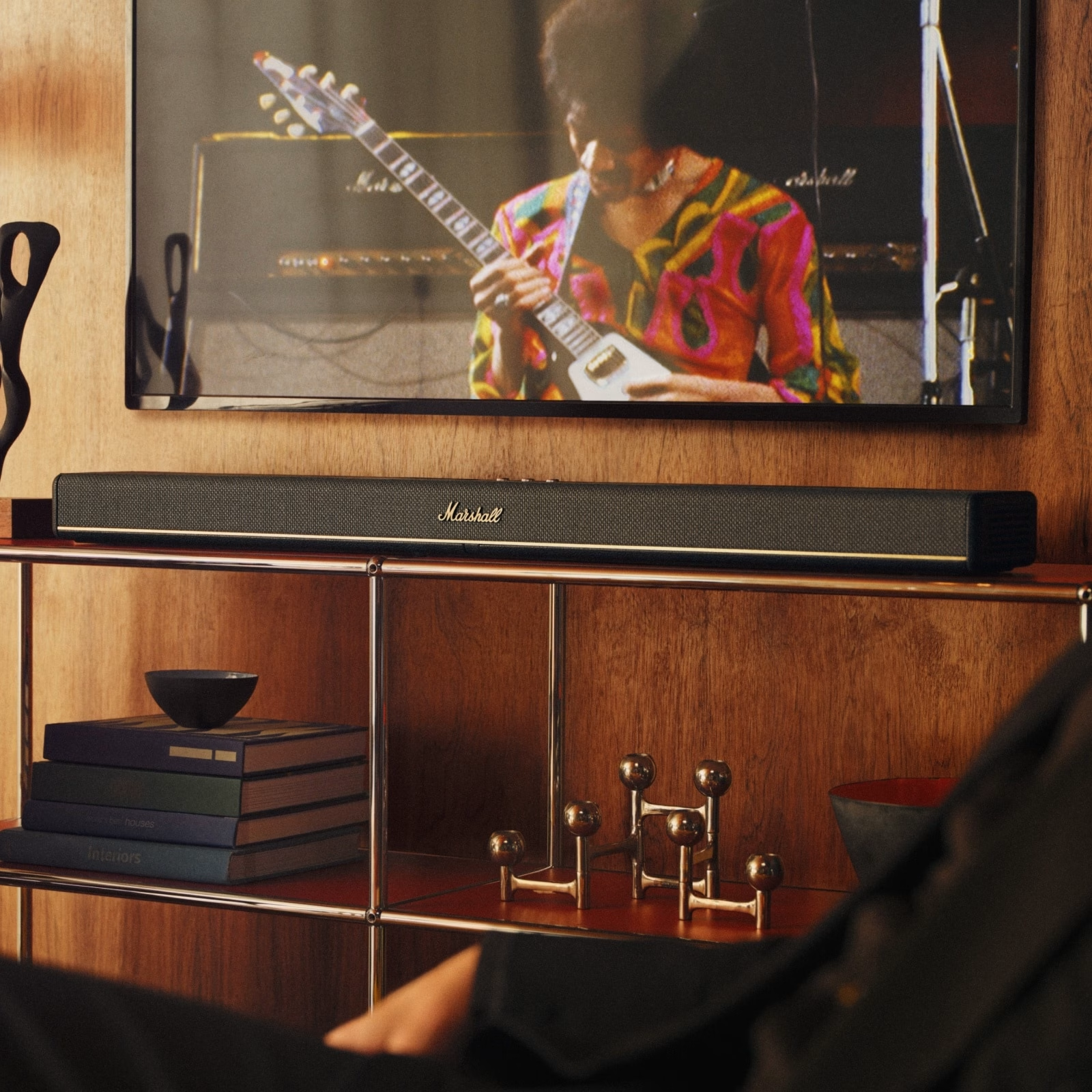 Ein Fernseher mit Gitarrist, eine Marshall-Soundbar, Bücher, eine Schüssel und dekorative Gegenstände auf Holzregalen.