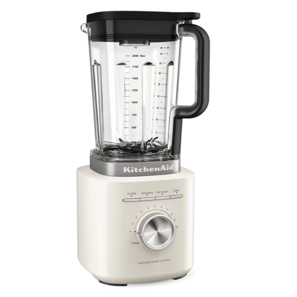 Egy KitchenAid turmixgép. Fehér alappal rendelkezik, a sebességszabályozó tárcsával. Az üvegkancsón mérőjelek és fekete fedél található.