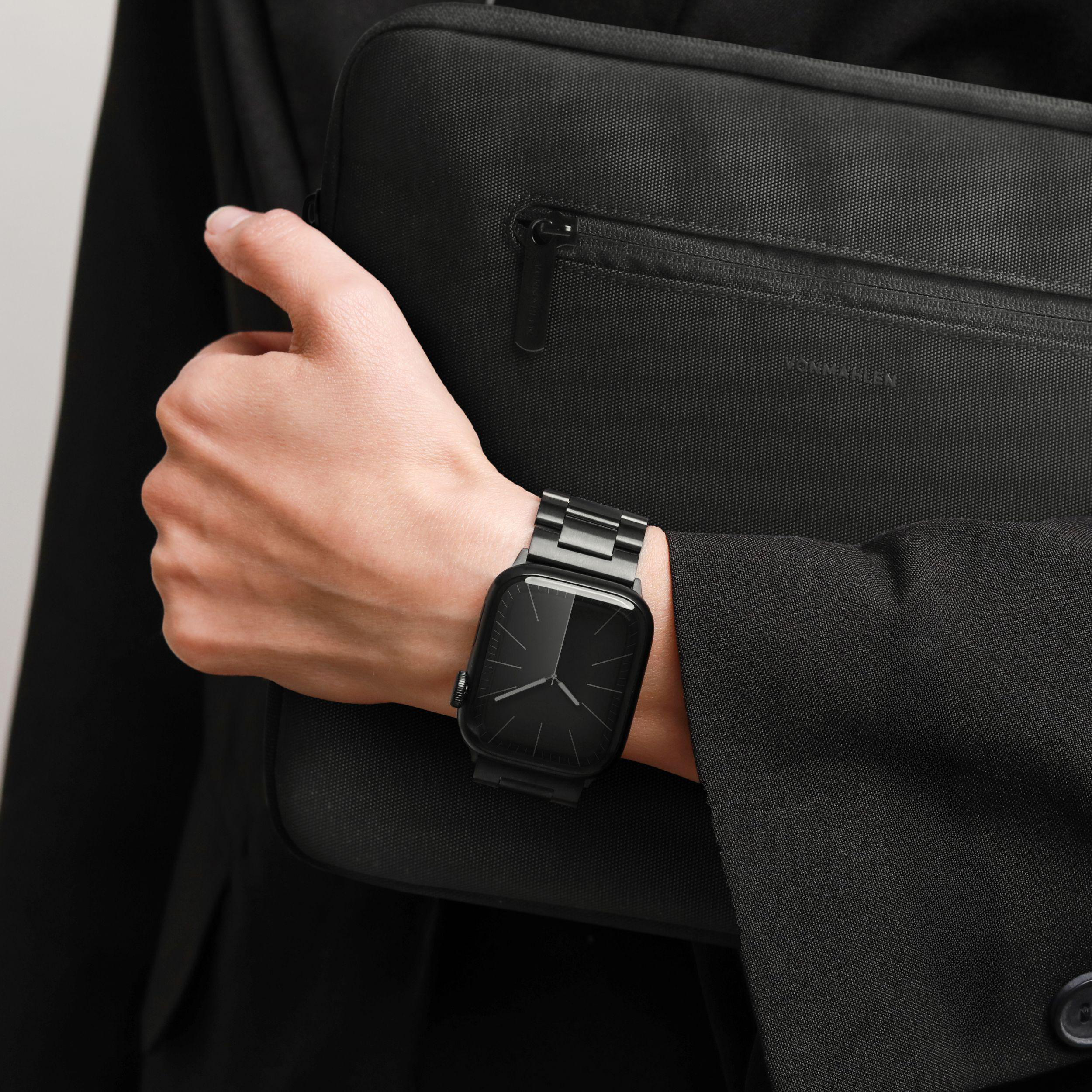 Eine Person mit schwarzer Uhr und Tasche. Die Person trägt einen schwarzen Anzug.