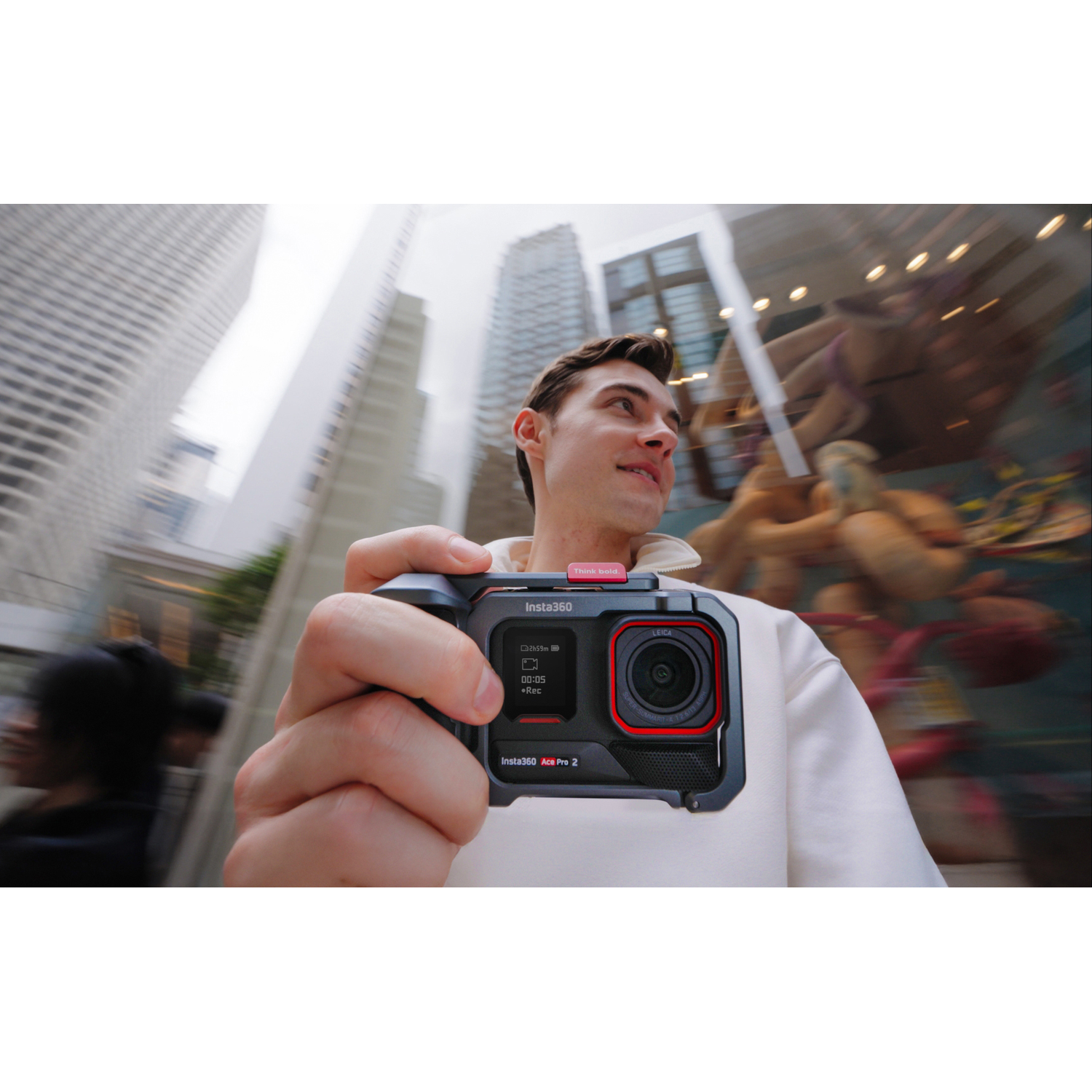 Homme tenant une caméra Insta360 noire avec des accents rouges, souriant, devant un fond urbain flou.
