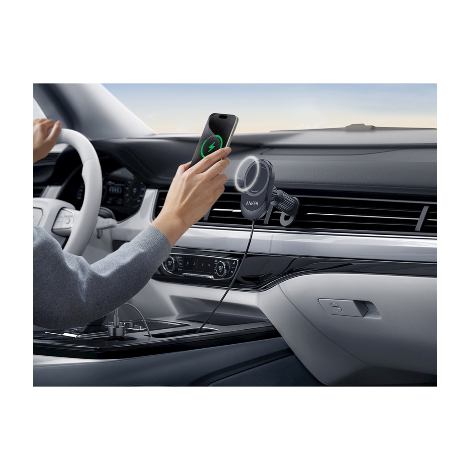 Una persona tiene in mano un telefono con un'icona di ricarica in un'auto. Supporto per telefono Anker visibile. L'interno dell'auto è a fuoco.
