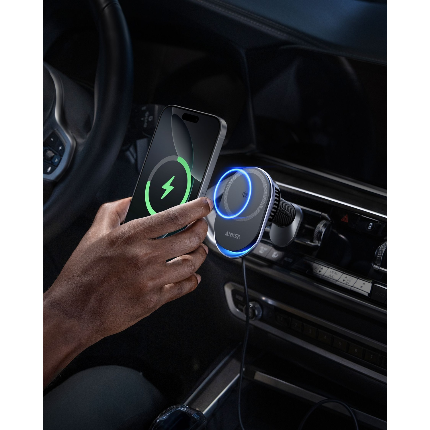 Una mano tiene un telefono sopra un caricatore per auto wireless. Il telefono mostra un simbolo di carica. Il caricatore è di Anker.