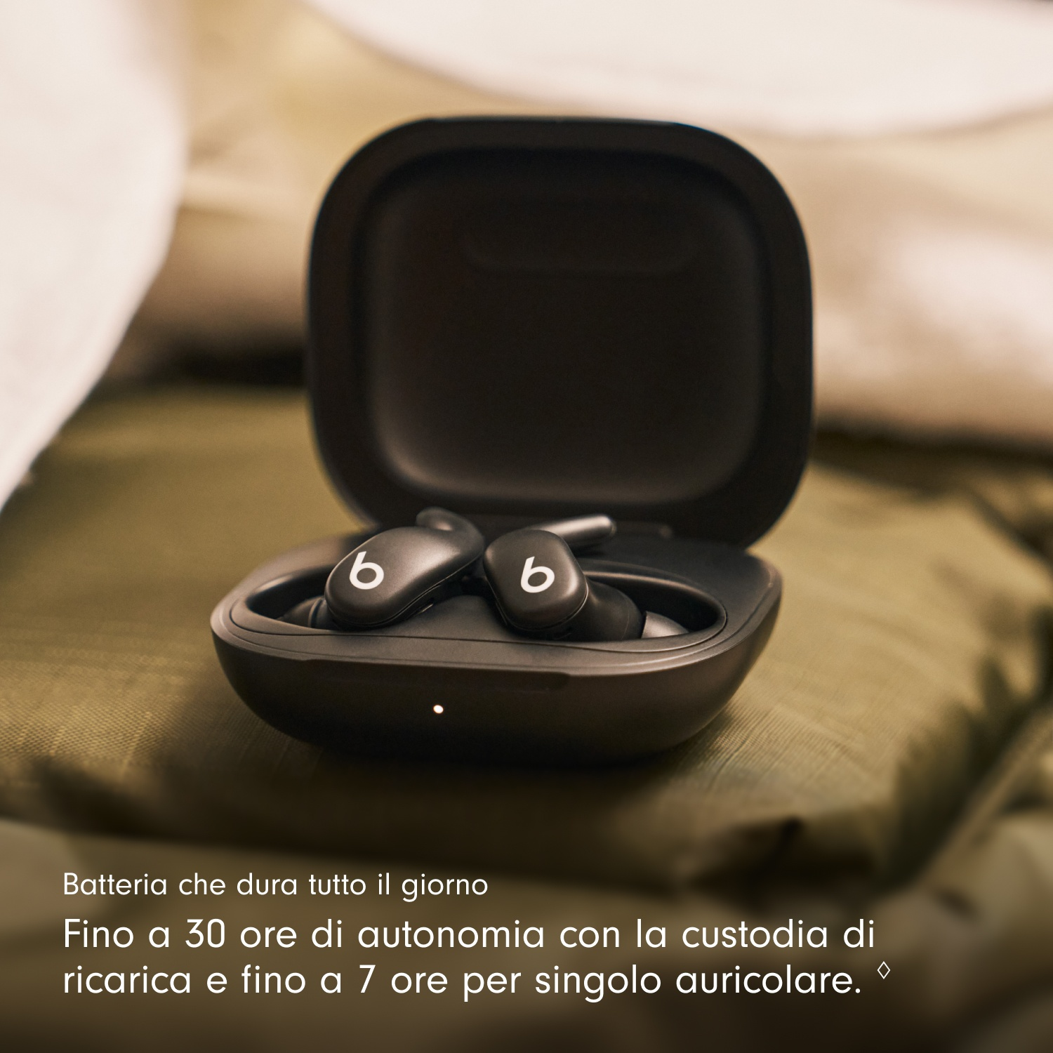 Auricolari Beats neri in una custodia di ricarica aperta, su una superficie verde. Testo bianco: Batteria che dura tutto il giorno.