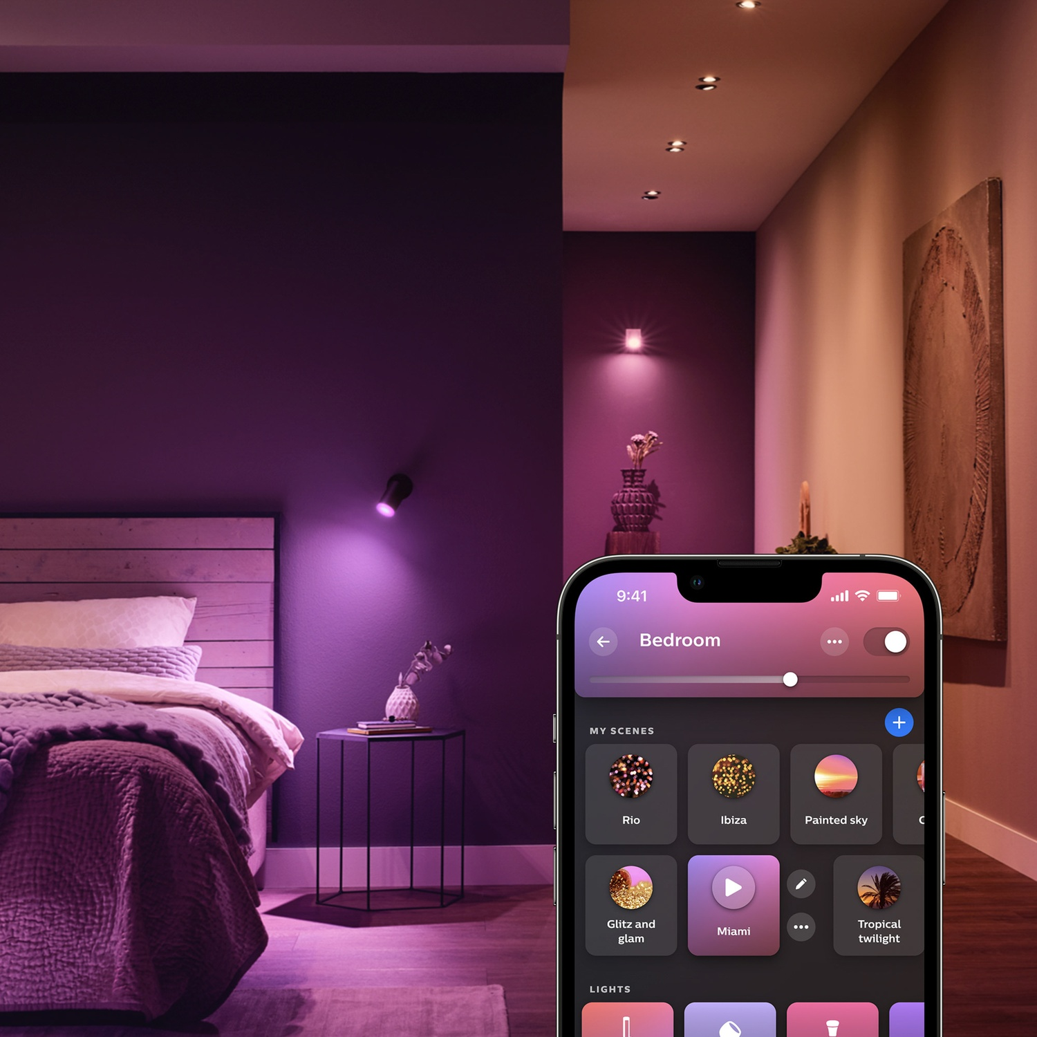 A bedroom scene with purple lighting. A bed, side table, and smartphone displaying a room lighting control app are visible.