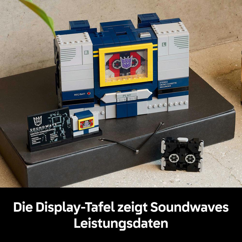 Ein Lego Soundwave-Spielzeug, ein Transformer, steht auf einer schwarzen Oberfläche. Es enthält ein Display und eine kleine Kassette.