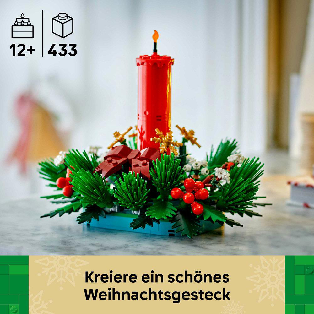 Ein Lego-Weihnachtsgesteck. Rote Kerze mit Flamme, umgeben von grünem Laub, roten Beeren und goldenen Akzenten. Auf einem Tisch.
