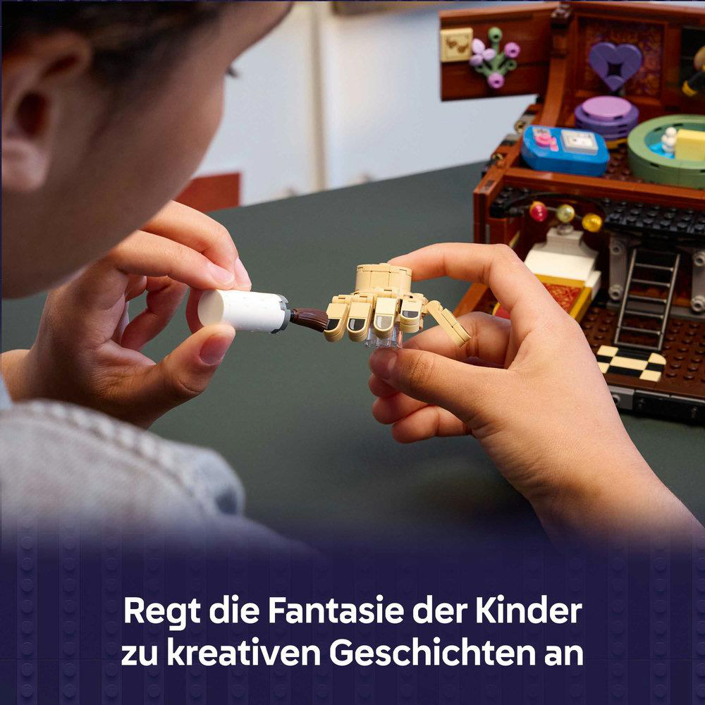 Eine Person setzt eine beige Lego-Hand mit einem weißen Teil zusammen. Im Hintergrund befindet sich eine hölzerne Schatzkiste.