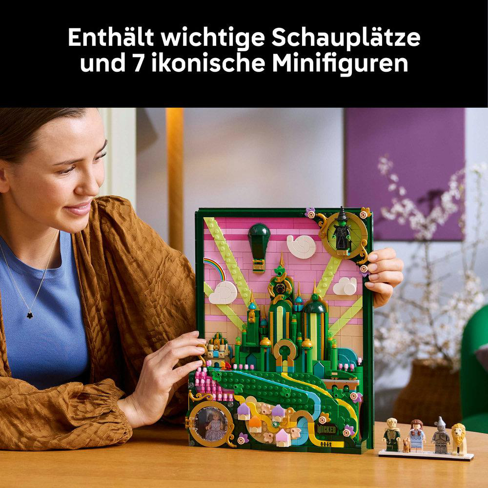 Eine Frau hält ein LEGO-Set mit Szenen aus dem Zauberer von Oz. Das Set enthält Minifiguren und eine detaillierte Smaragdstadt.