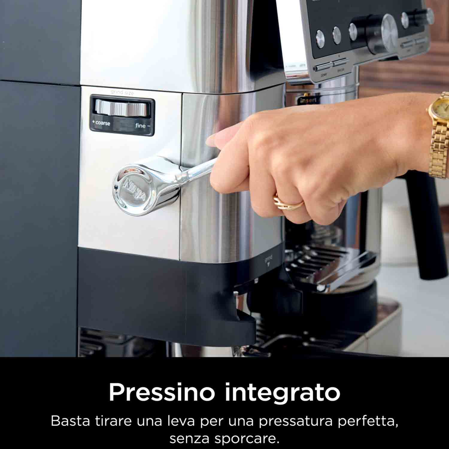 La mano di una persona tira una leva su una macchina da caffè Ninja. La macchina è argento e nera, con la scritta 'Pressino integrato'.