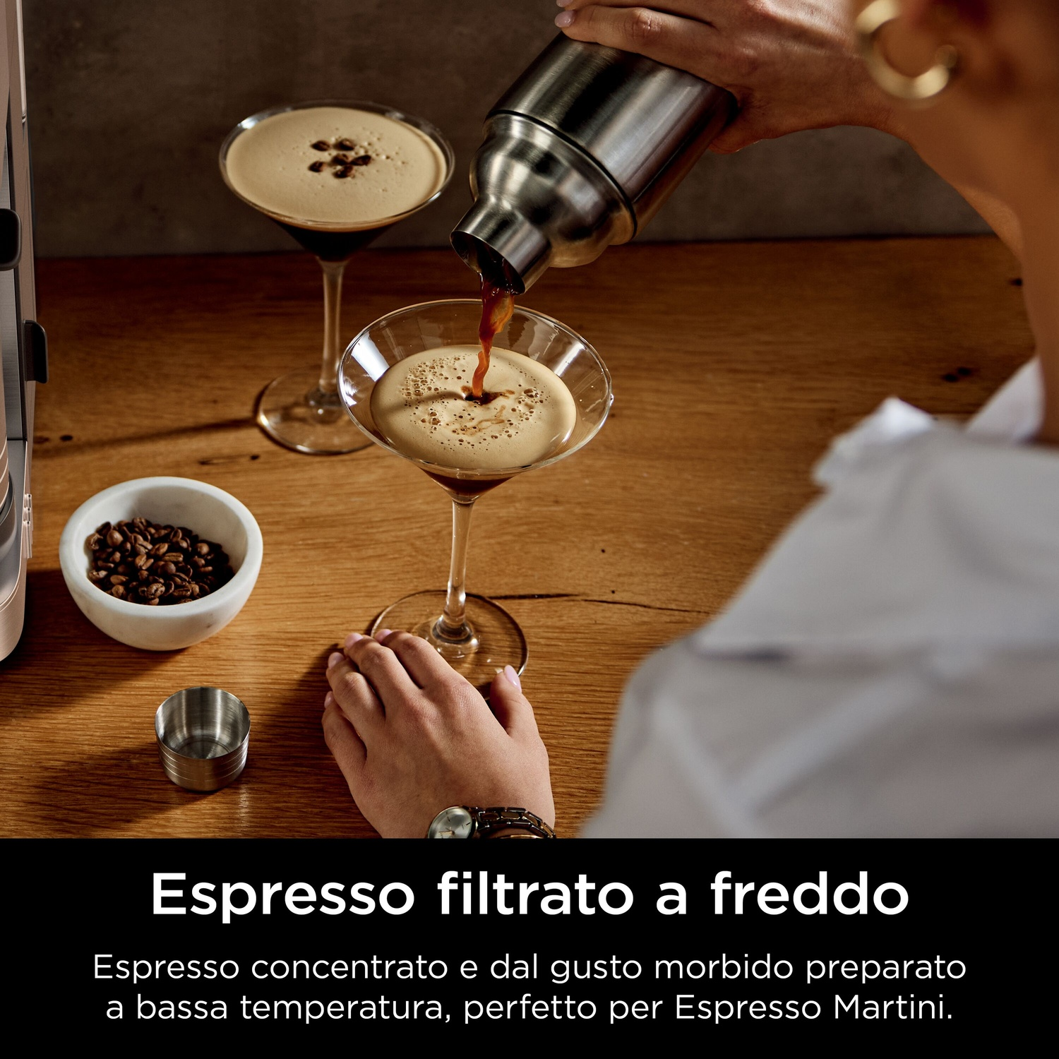 Una persona versa l'espresso in un bicchiere da martini. Due bicchieri con caffè su un tavolo di legno. Chicchi di caffè in una ciotola.