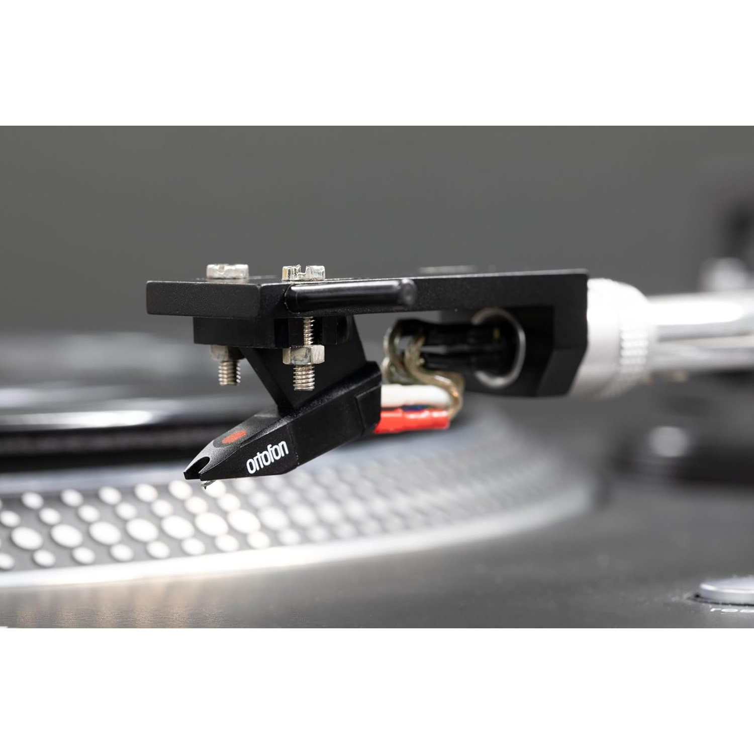 Primo piano di uno stilo nero per giradischi con il marchio 'ortofon' visibile. È posizionato sopra un giradischi argentato.