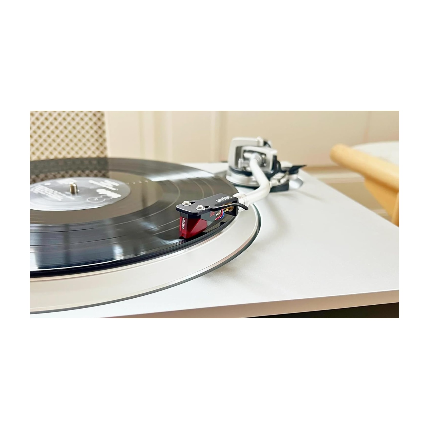 Un giradischi riproduce un disco in vinile. La puntina è sul disco, il braccio è visibile. Il giradischi è su una superficie bianca.