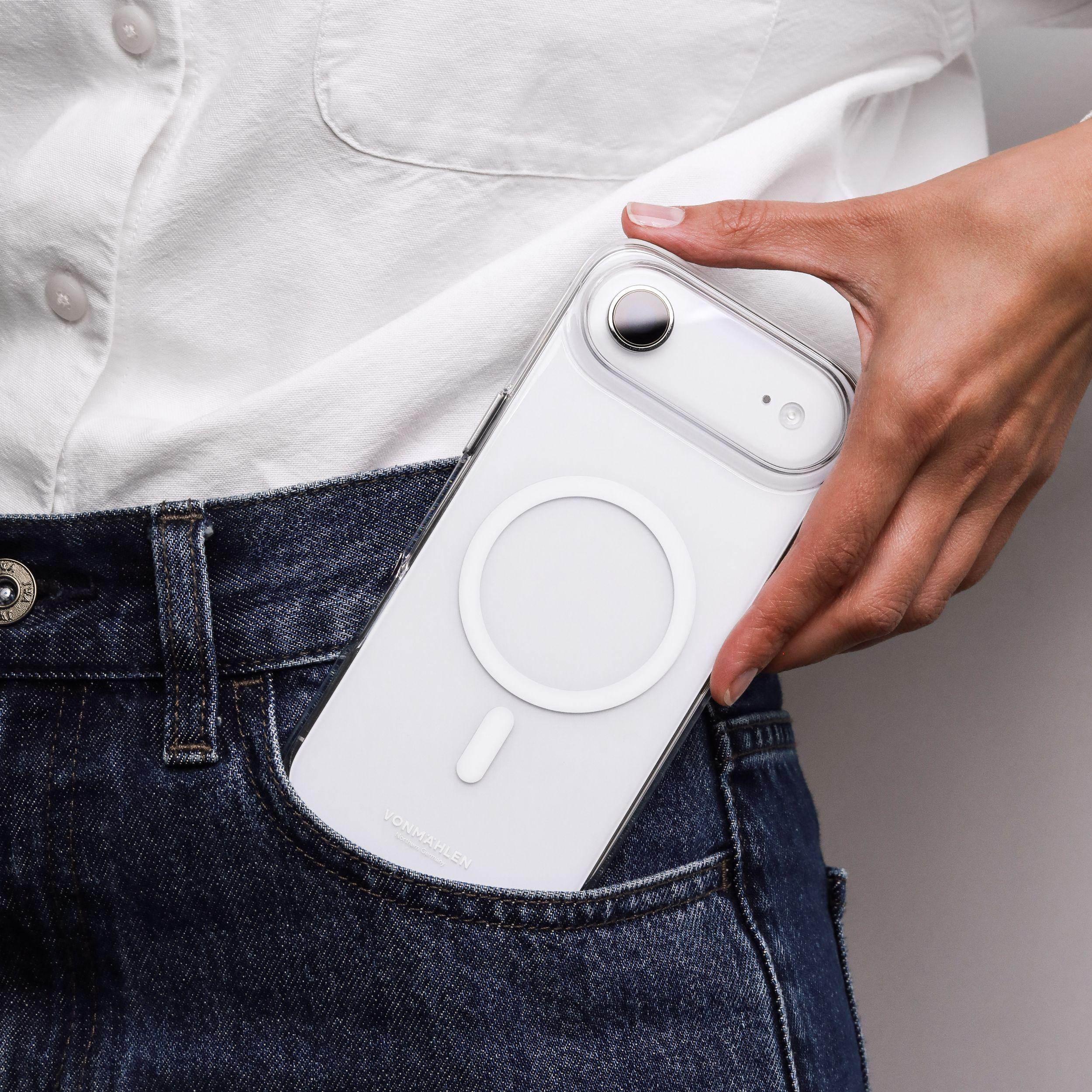 Eine Hand hält ein weißes Telefon in einer Jeanstasche. Das Telefon hat eine transparente Hülle. Der Hintergrund ist ein weißes Hemd.