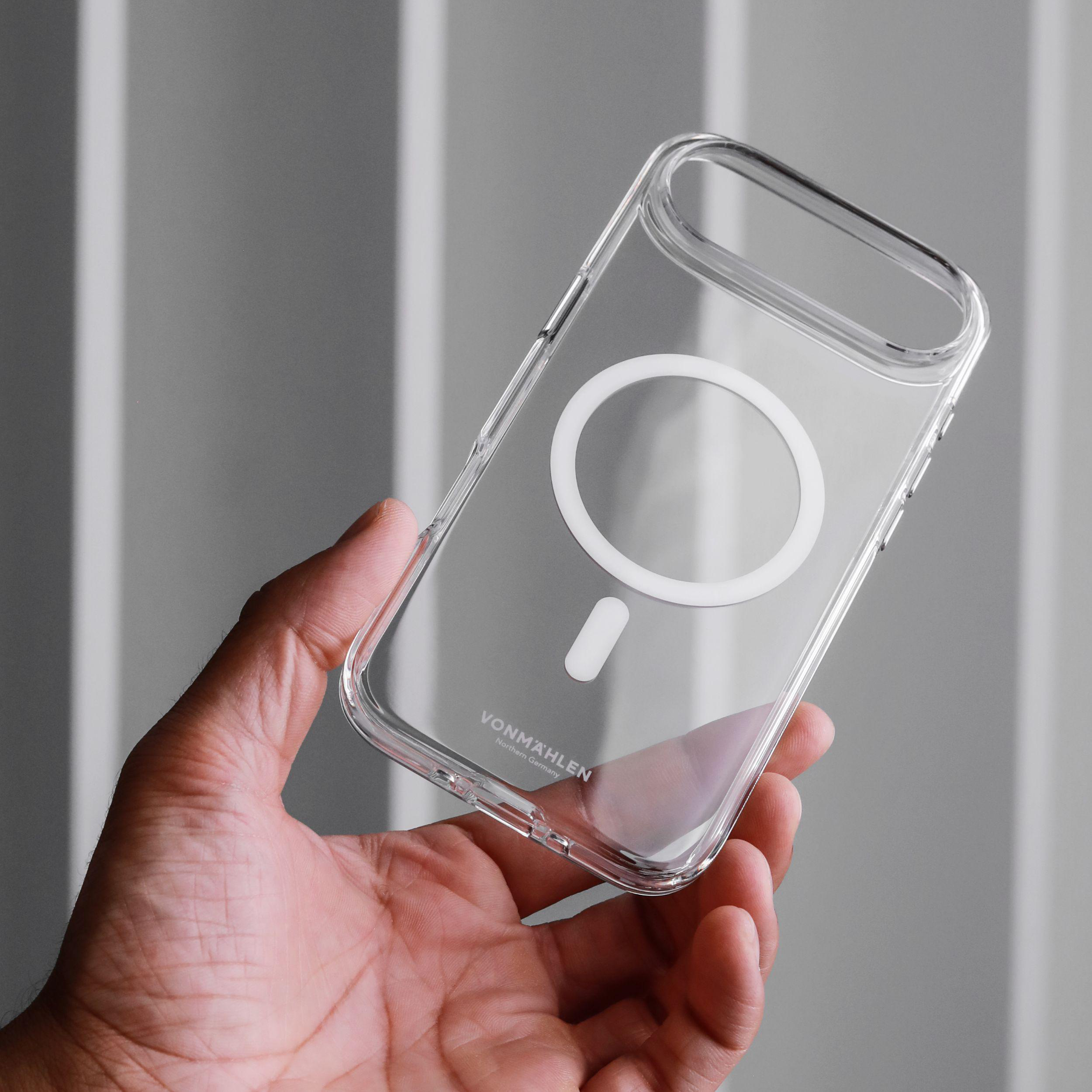 Eine Hand hält eine transparente Handyhülle mit einem weißen MagSafe-Ring und Logo. Der Hintergrund ist hellgrau.
