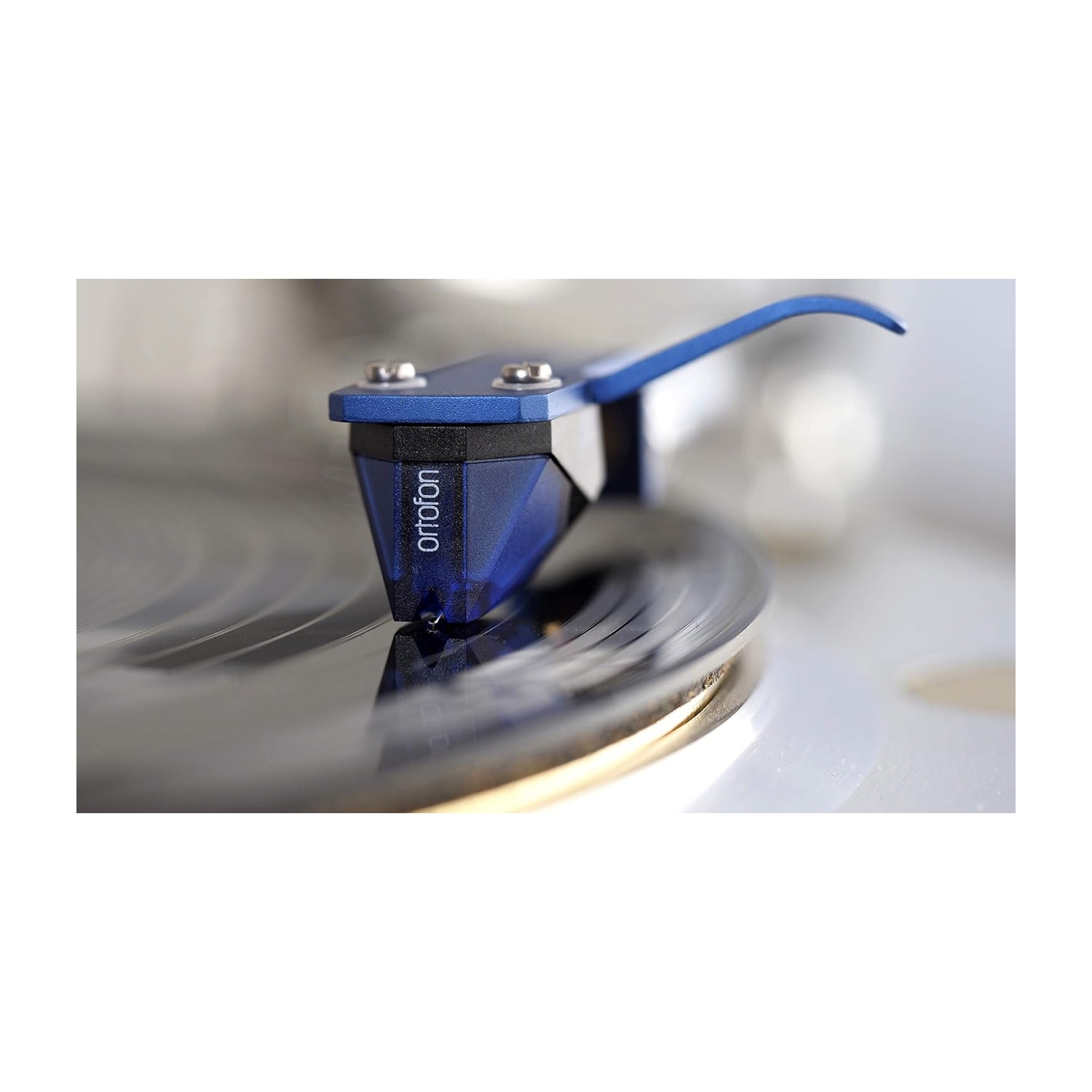 Uno stilo Ortofon blu su un giradischi. L'ago tocca un disco in vinile rotante. Lo sfondo è sfocato.