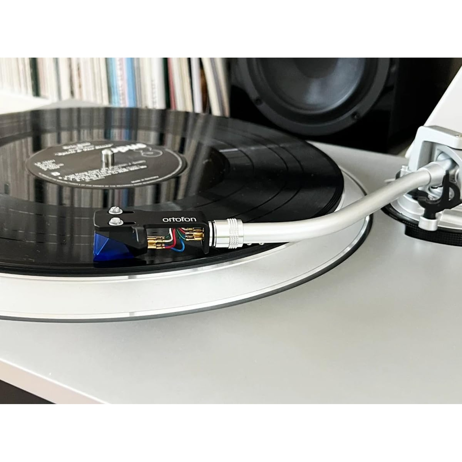 Un giradischi con un disco in vinile nero. L'ago è sopra il disco. Libri e un altoparlante sullo sfondo.