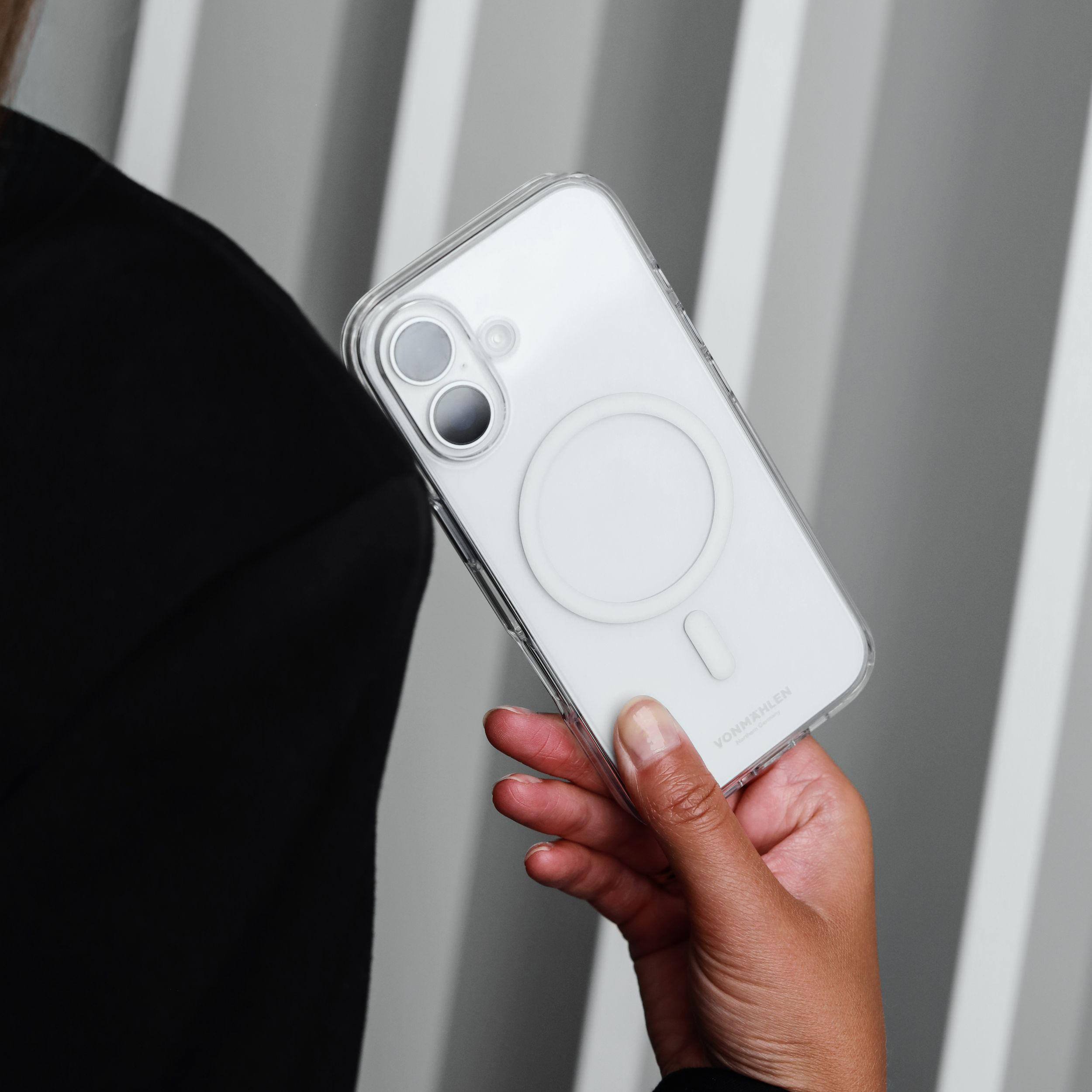 Eine Hand hält eine transparente Handyhülle mit einem weißen iPhone. Der Hintergrund sind vertikale weiße und graue Streifen.