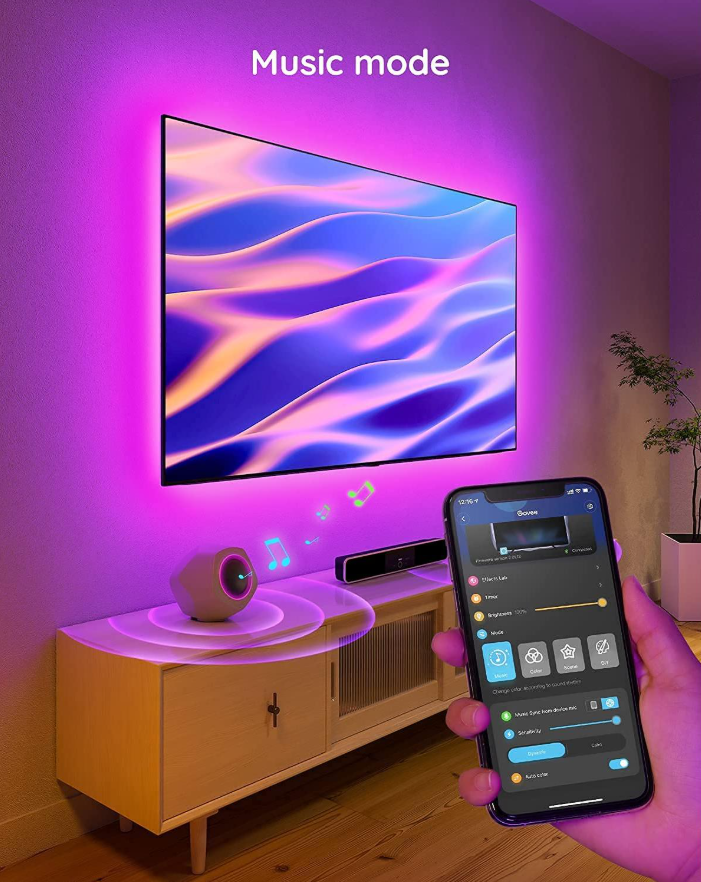 Una TV con luci viola intorno. Un altoparlante, un telefono e un mobile. Il telefono mostra un'app. La stanza ha una sfumatura viola.