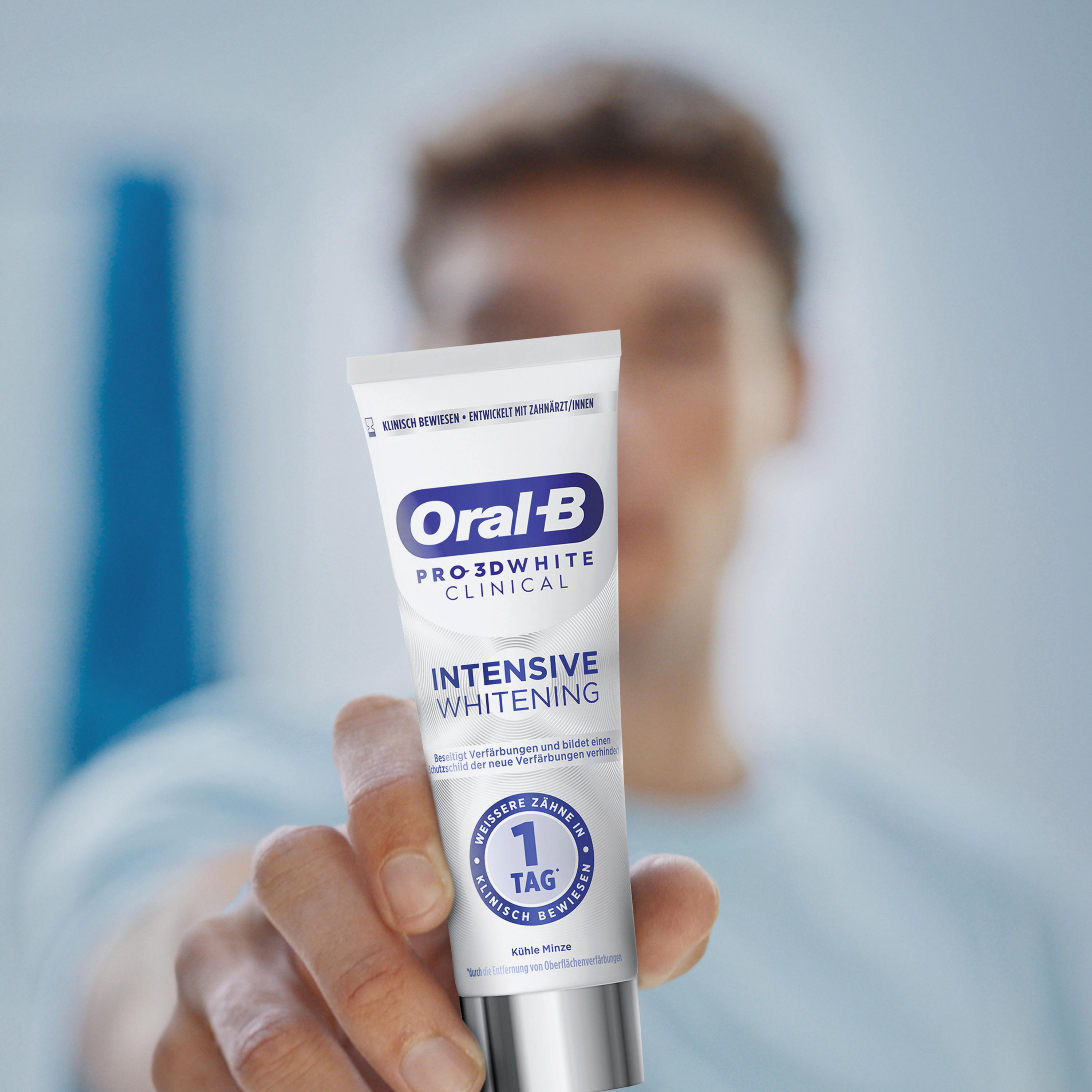 Eine Person hält eine Tube Oral-B Pro-3D White Zahnpasta. Die Tube ist weiß mit blauen und violetten Akzenten.