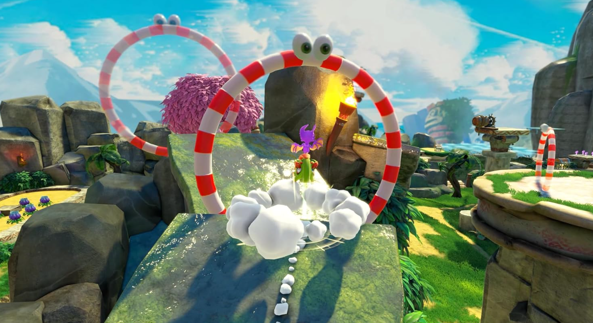 Ein lila Drache fliegt auf einen rot-weiß gestreiften Reifen mit Augen zu. Die Szene ist eine bunte Spielelandschaft mit Wolken.