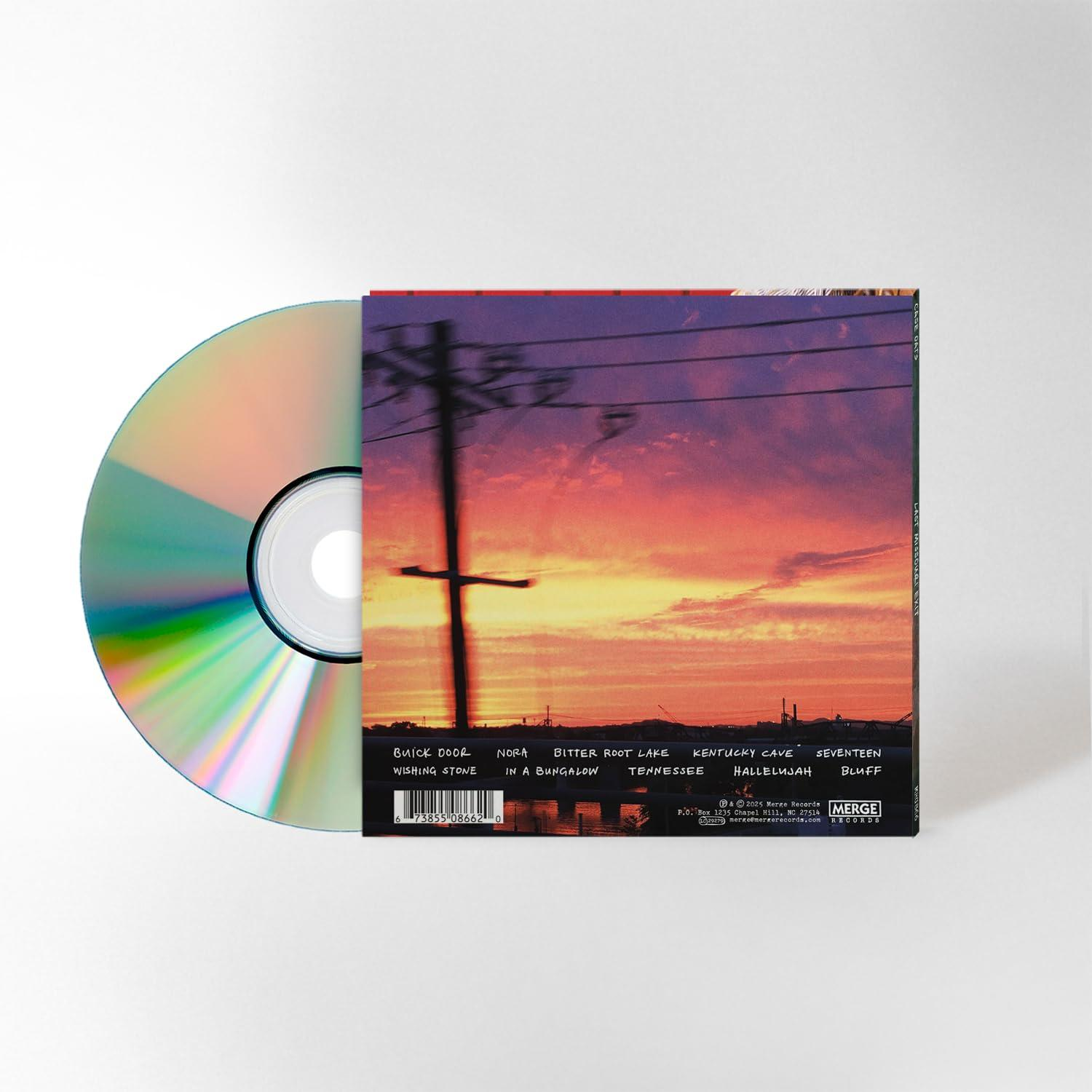 Eine CD liegt neben ihrer Hülle. Die Hülle zeigt einen Sonnenuntergang, Stromleitungen und Text. Die CD ist silberfarben.