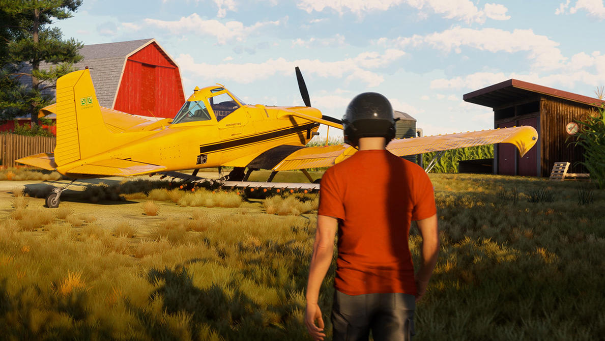 Ein Mann in einem orangefarbenen Hemd steht vor einem gelben Agrarflugzeug. Eine rote Scheune und ein Schuppen sind im Hintergrund sichtbar.