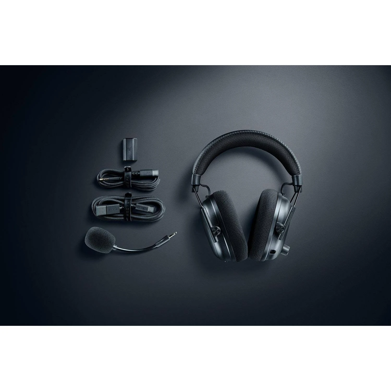 Auriculares gaming negros con accesorios: cables, micrófono y adaptador de carga. Todo sobre un fondo gris oscuro.