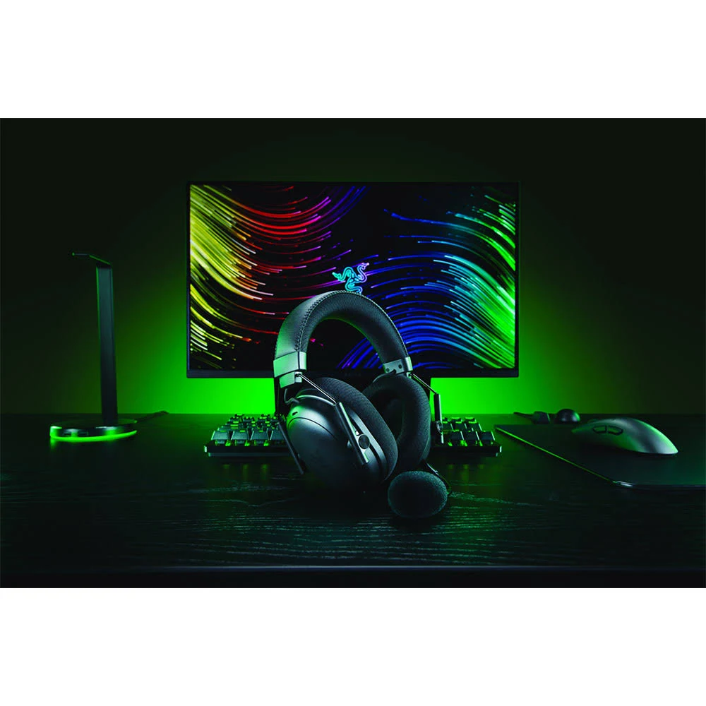 Una configuración de juego con auriculares en foco. Un monitor muestra líneas coloridas. Teclado, ratón y soporte también visibles.