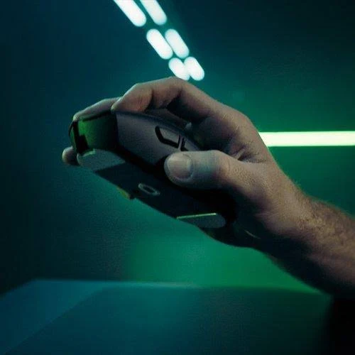 Una mano sosteniendo un ratón de ordenador negro. El fondo es verde con luces borrosas.
